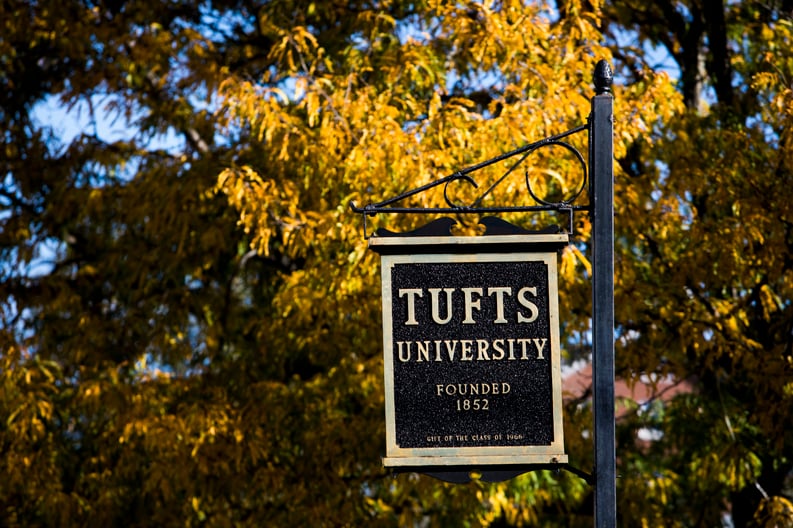 Photo of Tufts University street sign with fall foliage in background.